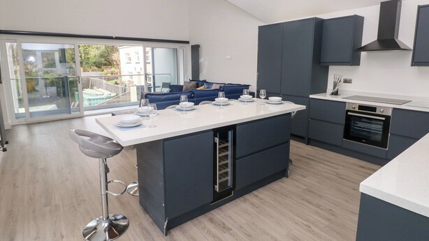 A modern kitchen with a central island, dark cabinetry, and a large window overlooking a balcony. - Milkwood Villa (Carmarthen)