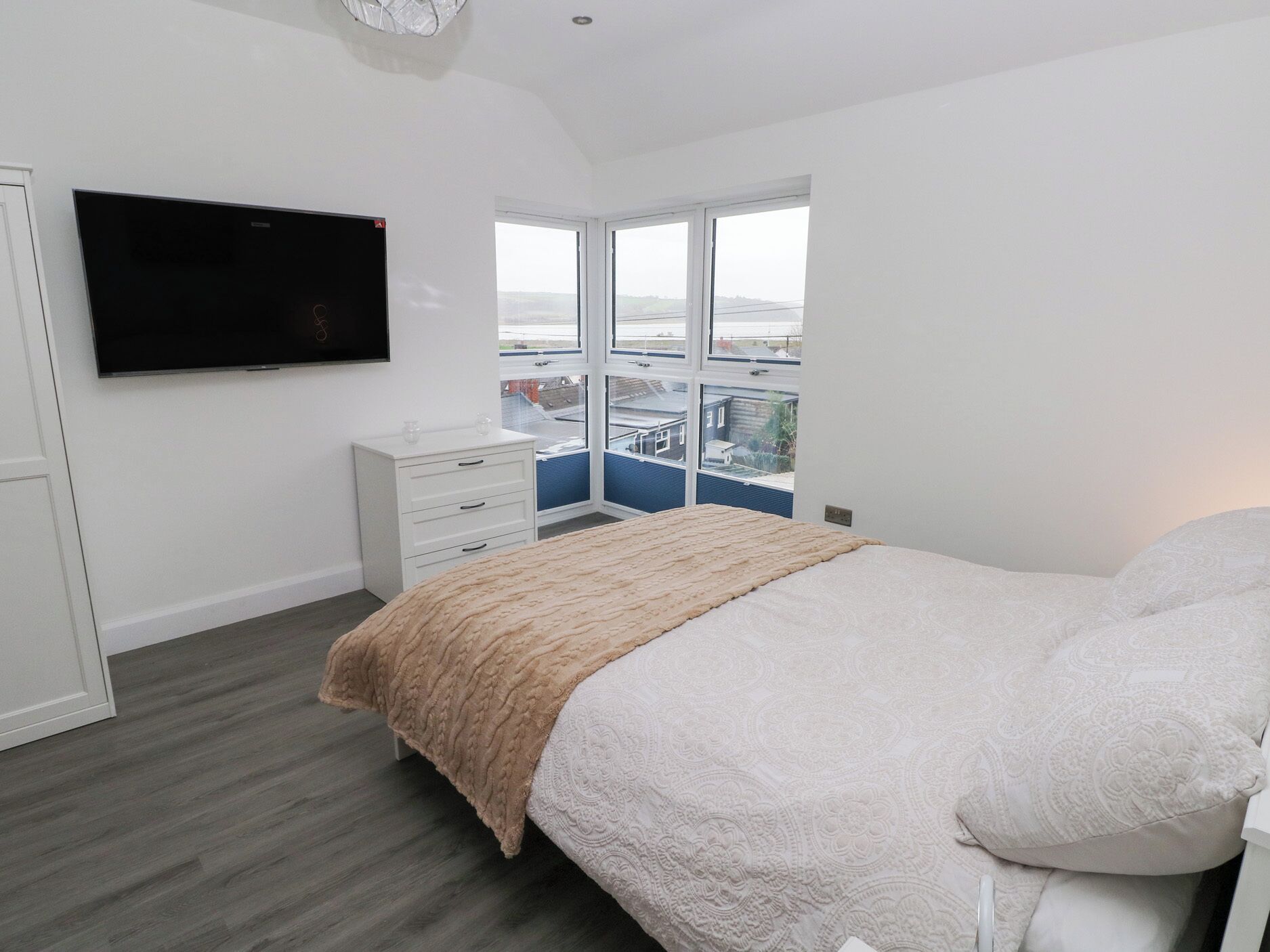 Un dormitorio con una cama, televisor, cómoda y ventana con vista a edificios.