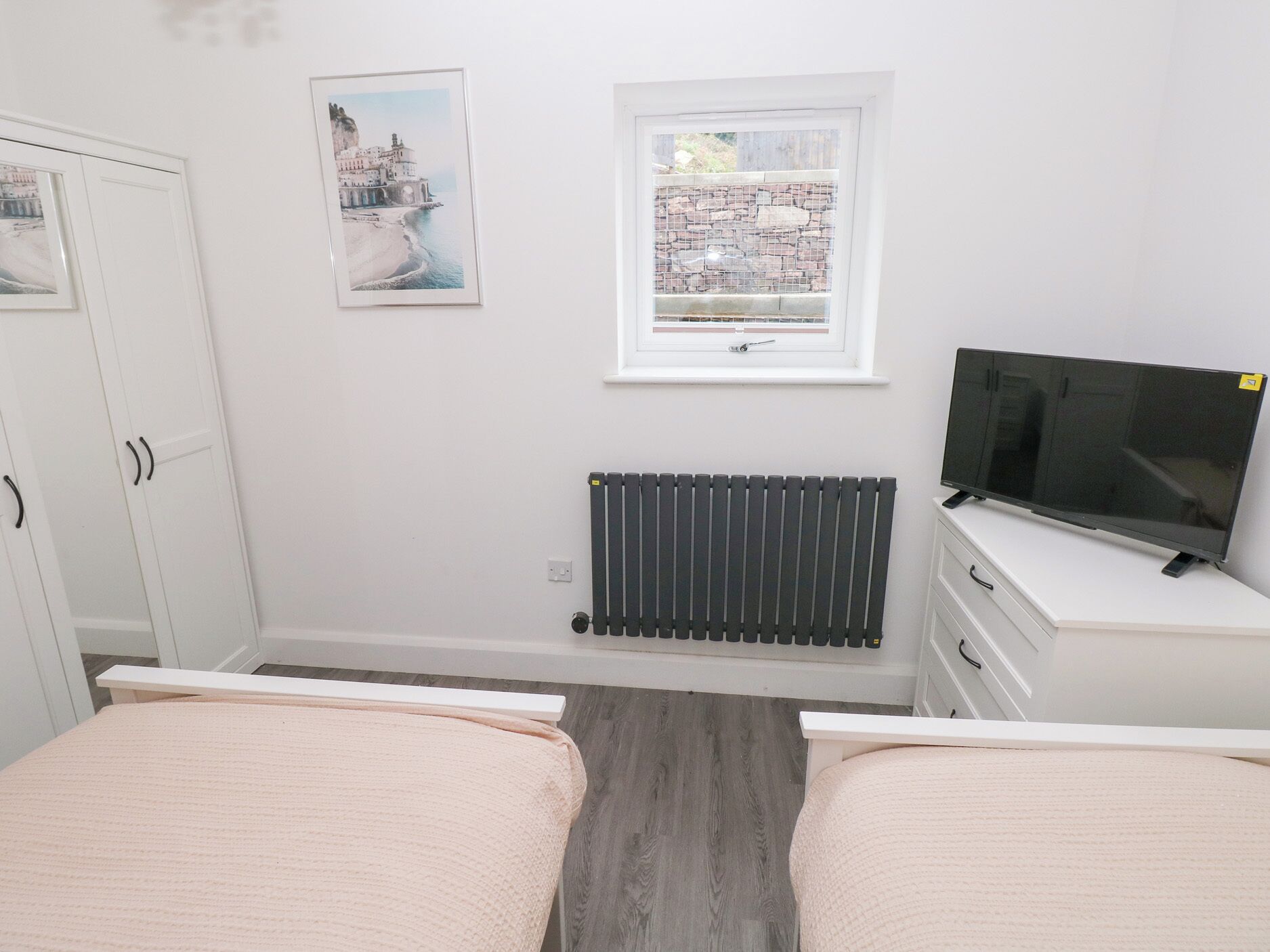 A bedroom with a bed, a TV, a radiator, a window with a view, and a wardrobe.