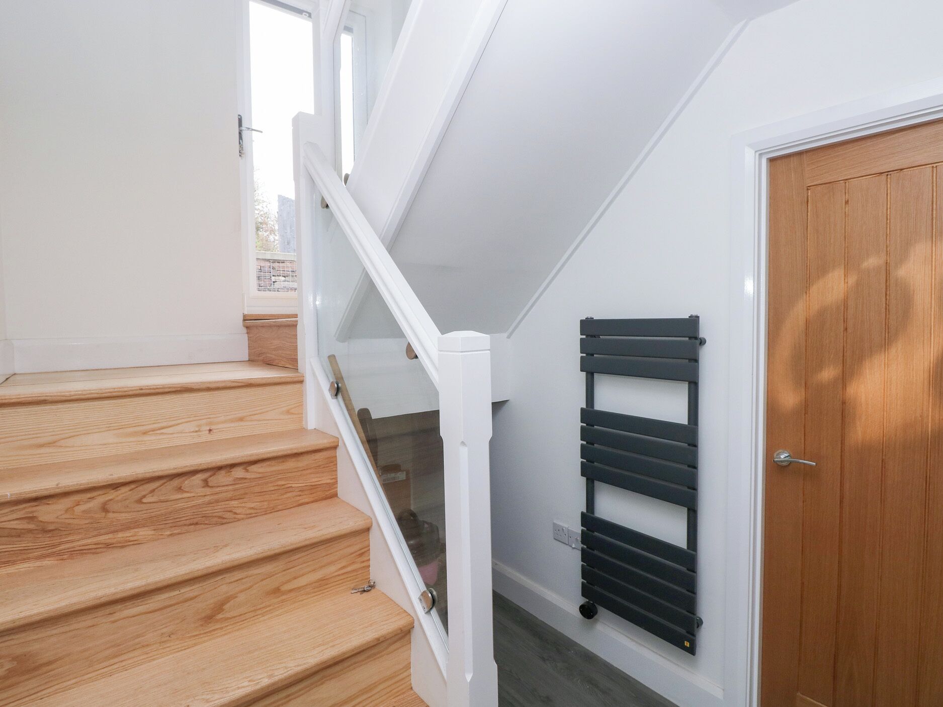 A staircase with wooden steps and white railings, a black radiator, and a wooden door.