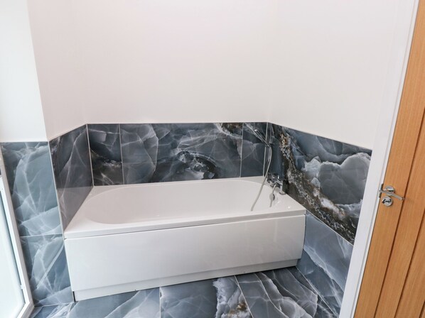 Ein Badezimmer mit einer weißen Badewanne, dunklen Marmorfliesen und einer Holztür.