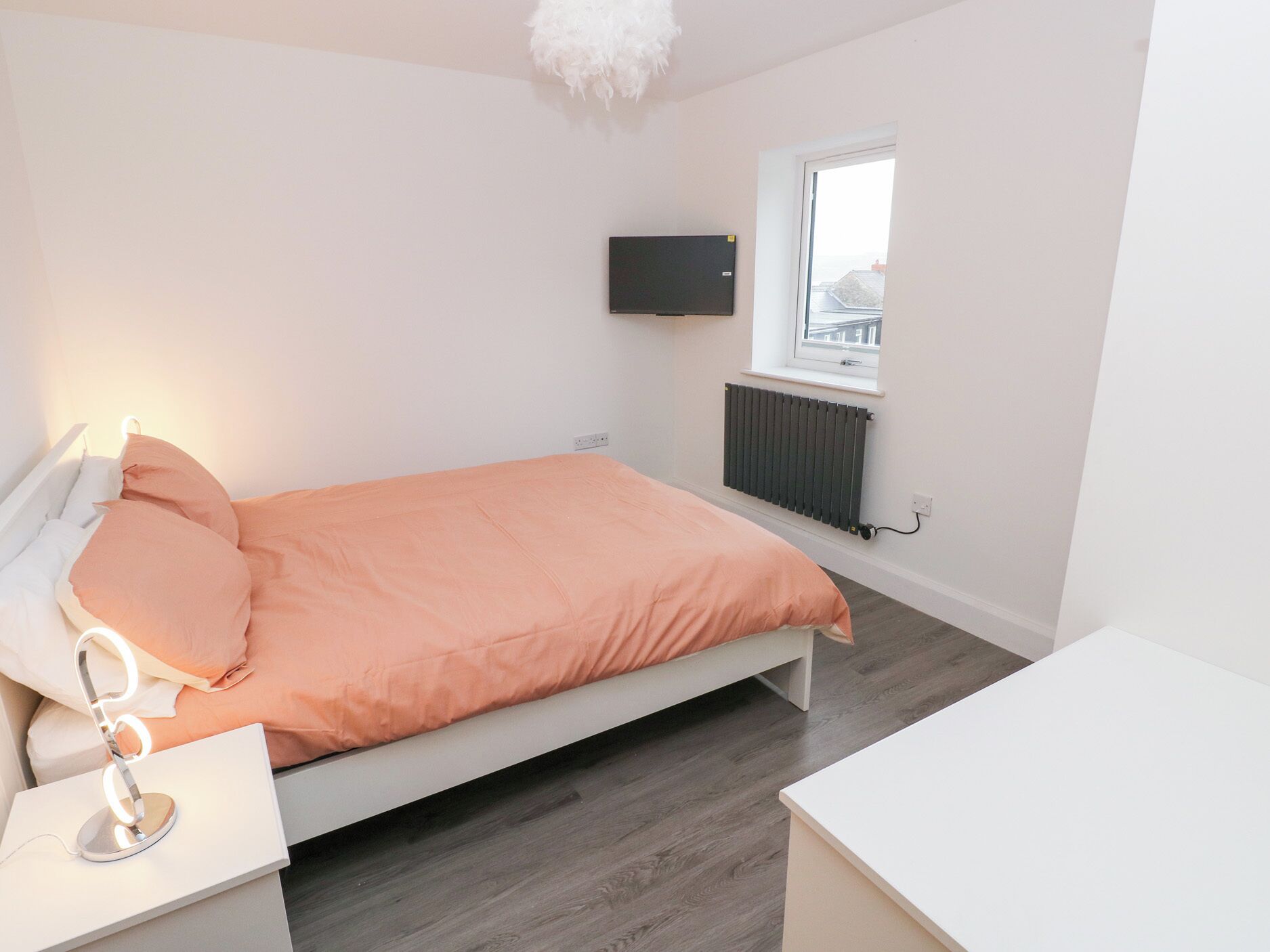 Un dormitorio con cama, mesita de noche y televisor montado en la pared.
