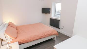 Un dormitorio con cama, mesita de noche y televisor montado en la pared.