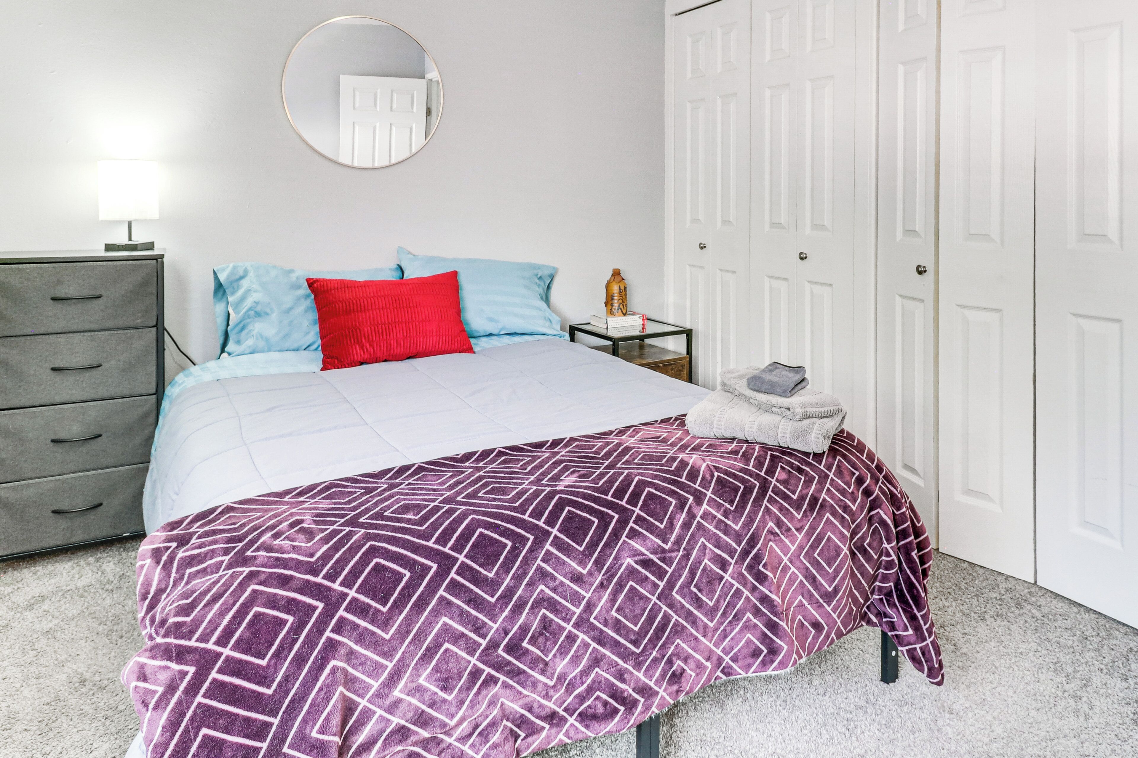 A bedroom with a bed, a dresser, a nightstand, a mirror, and a wardrobe.