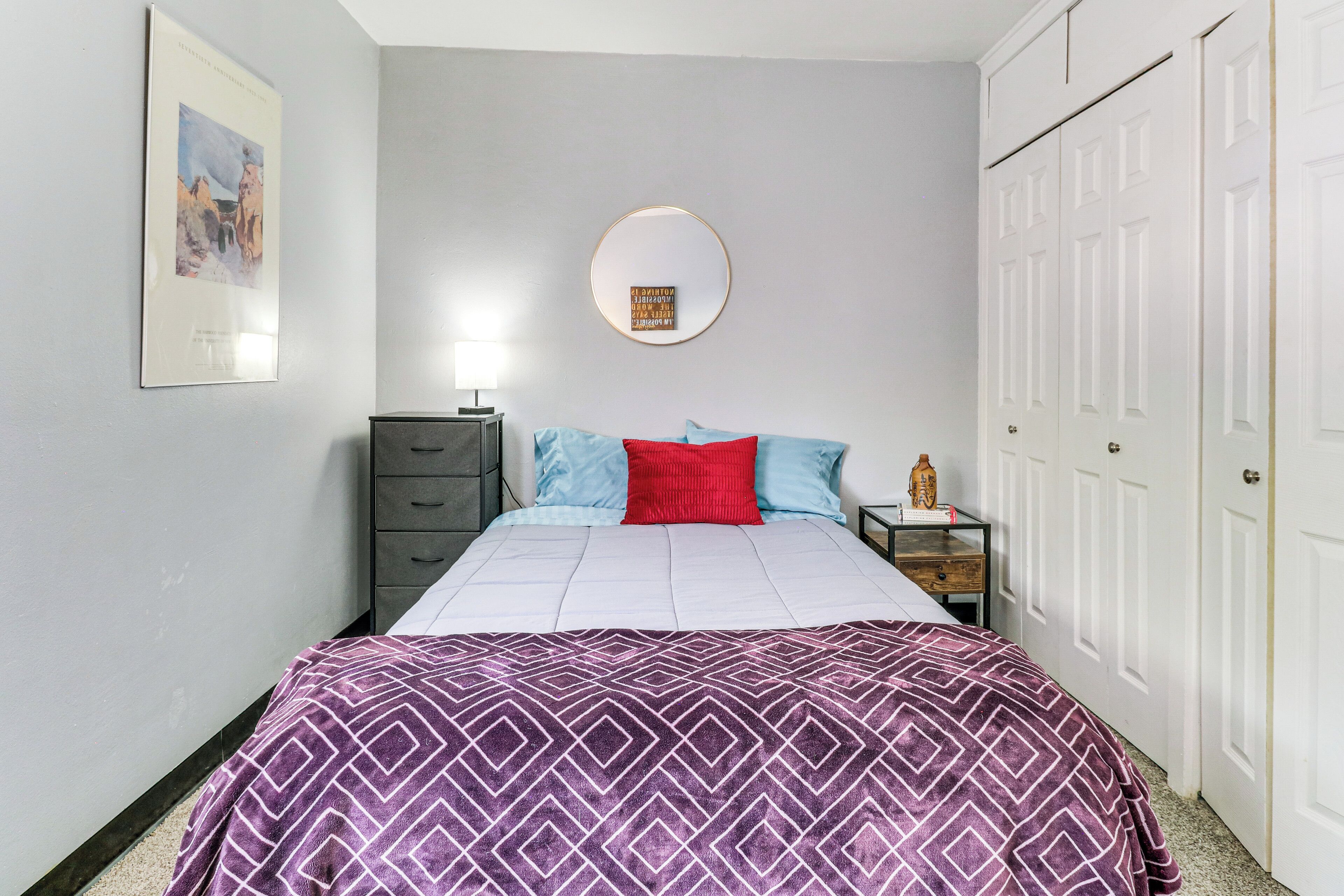 A bedroom with a bed, a dresser, a nightstand, a mirror, and a wardrobe.