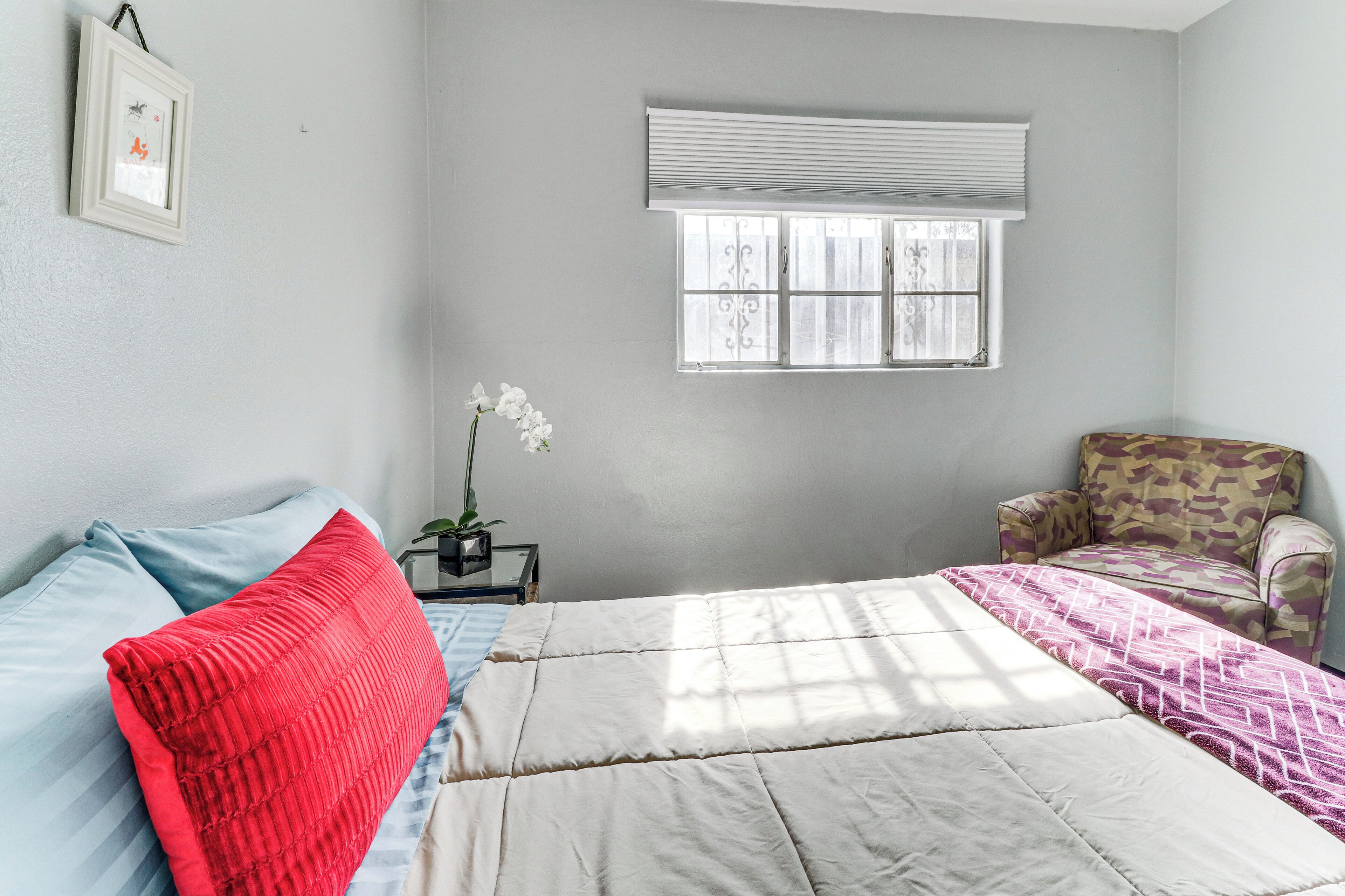 A bedroom with a bed, a chair, a window, and a framed picture on the wall.