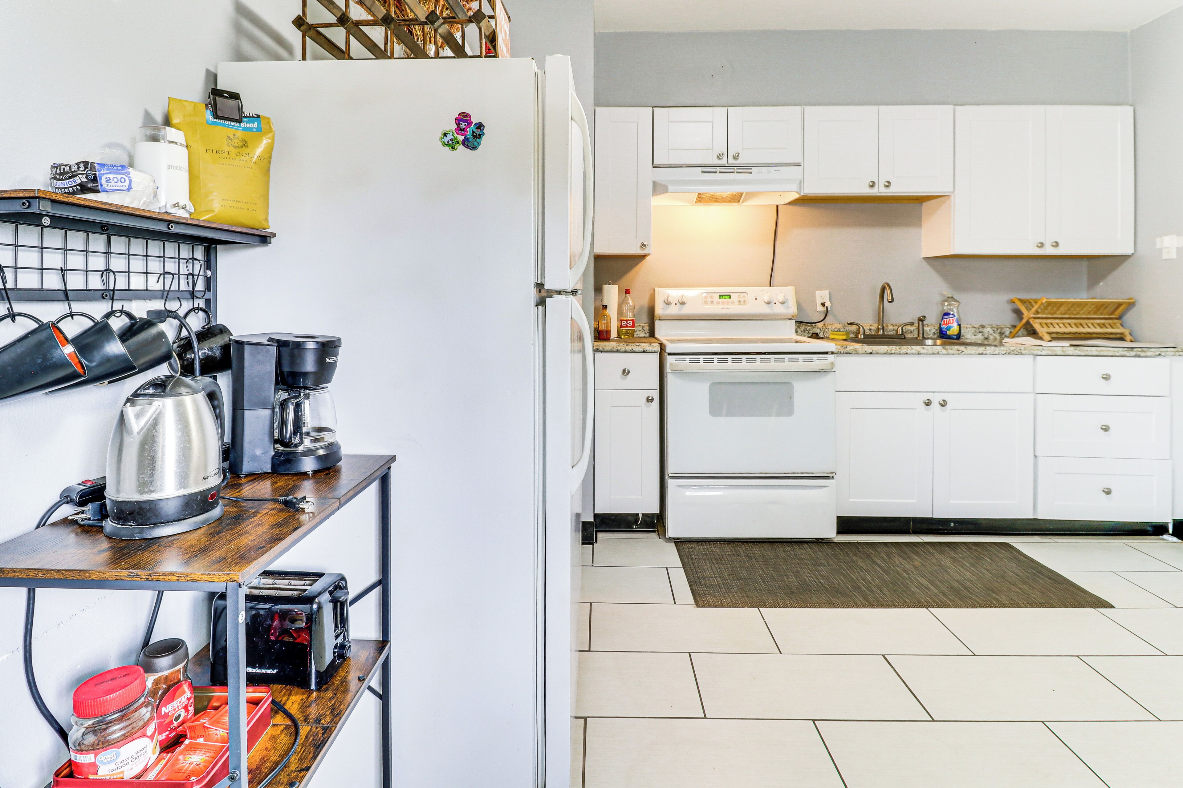 A kitchen with white cabinets, a stove, and a coffee maker on a wooden shelf.