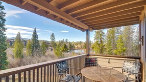 Un balcon couvert, agrémenté d’une table et de chaises, qui offre une vue sur un lac et une zone boisée.