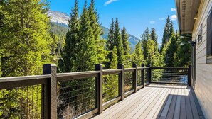 Eine Holzterrasse mit Metallgeländer, mit Blick auf eine bewaldete Landschaft und einen Berg.