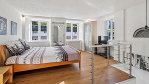 A modern bedroom with a wooden bed, a desk, and a TV. - Lodge of Sardona (Glarus Süd)