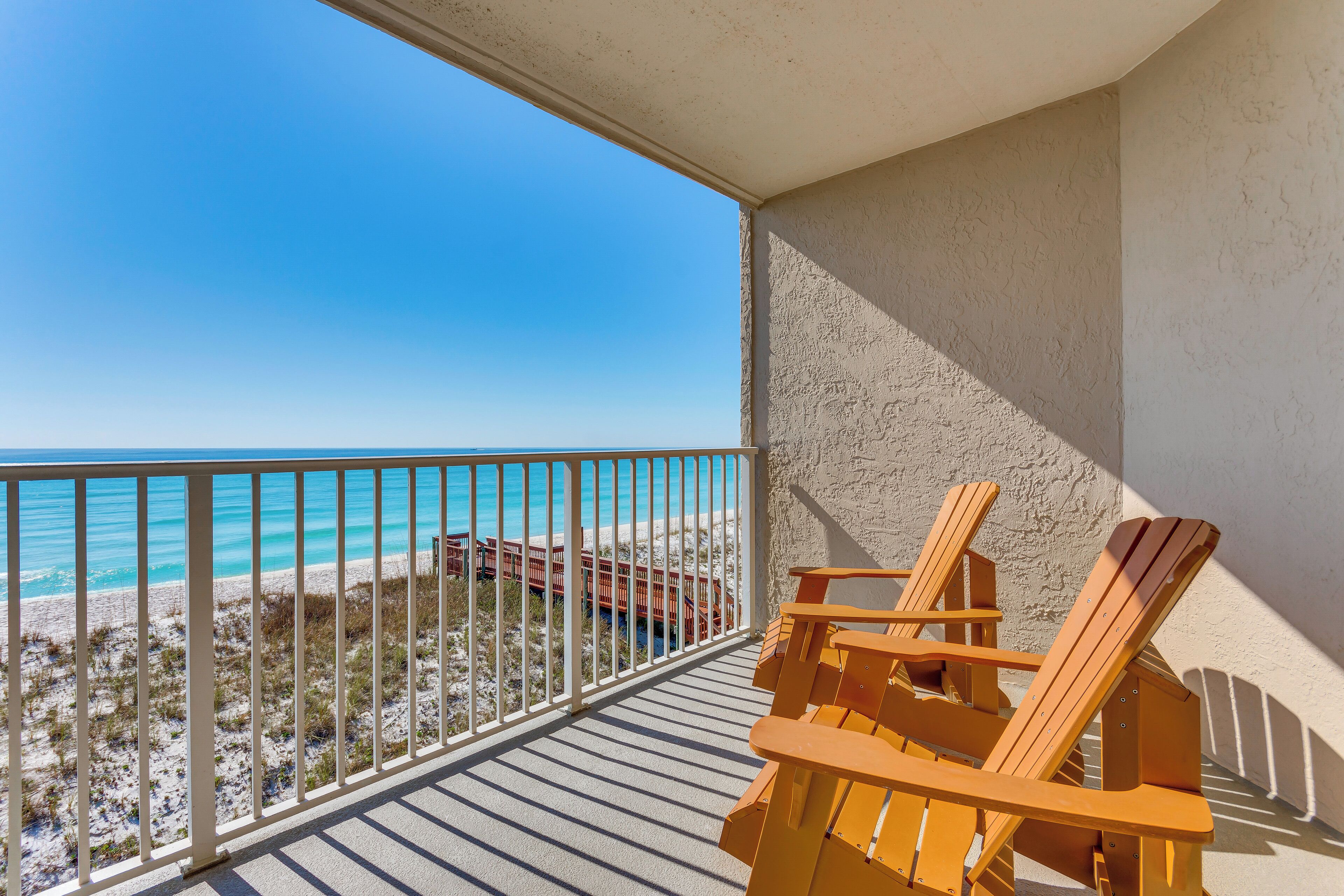 Un balcón con vista a la playa y al océano, sillas de madera y una barandilla.