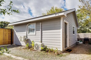 Une maison de plain-pied avec un petit porche à l’avant, une fenêtre et un appareil de climatisation fixé au mur extérieur.