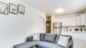 A modern living room with a grey sectional sofa, a small round table, and a wall-mounted washing machine. - Walk to Park: Dog-friendly Retreat in Pflugerville (Pflugerville)