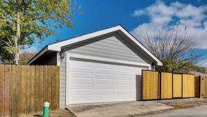 A garage with a white door, a wooden fence, and a green trash can. - Walk to Park: Dog-friendly Retreat in Pflugerville (Pflugerville)