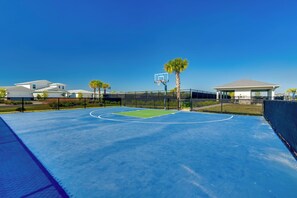 Una cancha de baloncesto al aire libre con un cielo azul despejado, rodeada de edificios residenciales y un pabellón cubierto.