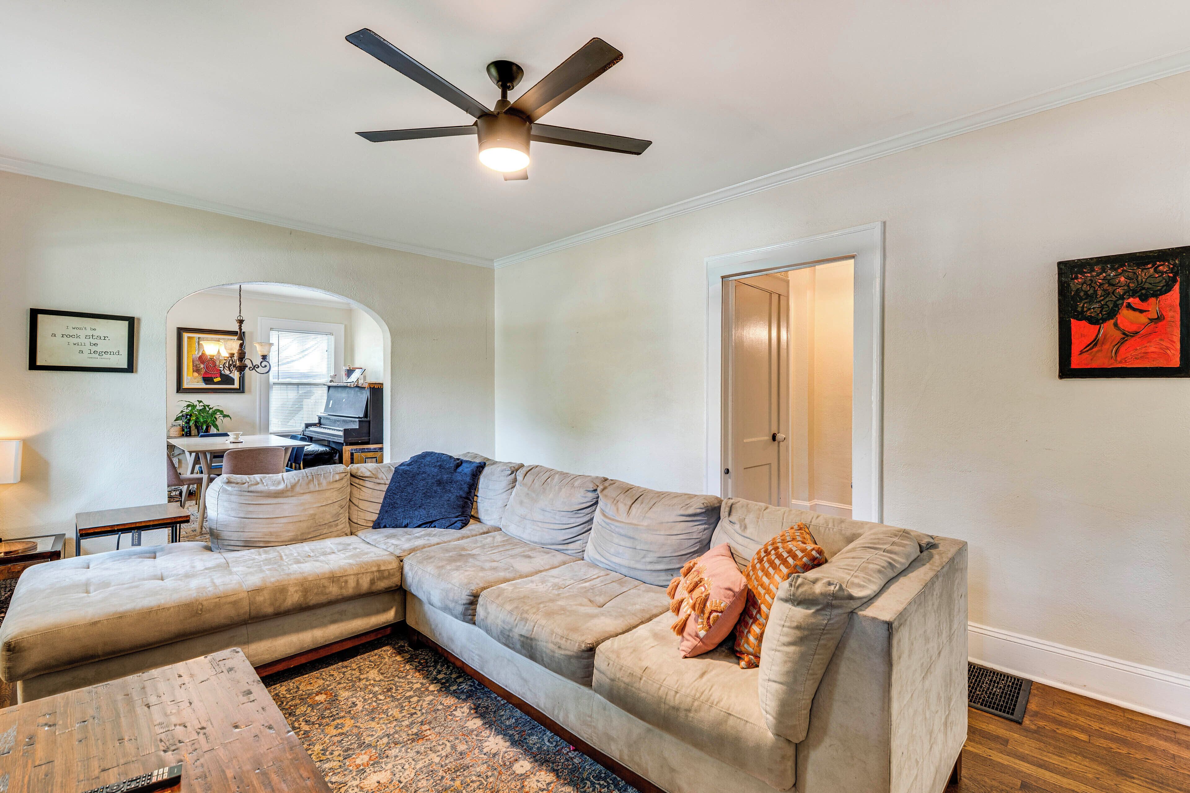 Un salon avec un canapé d’angle, un ventilateur de plafond et un tapis.
