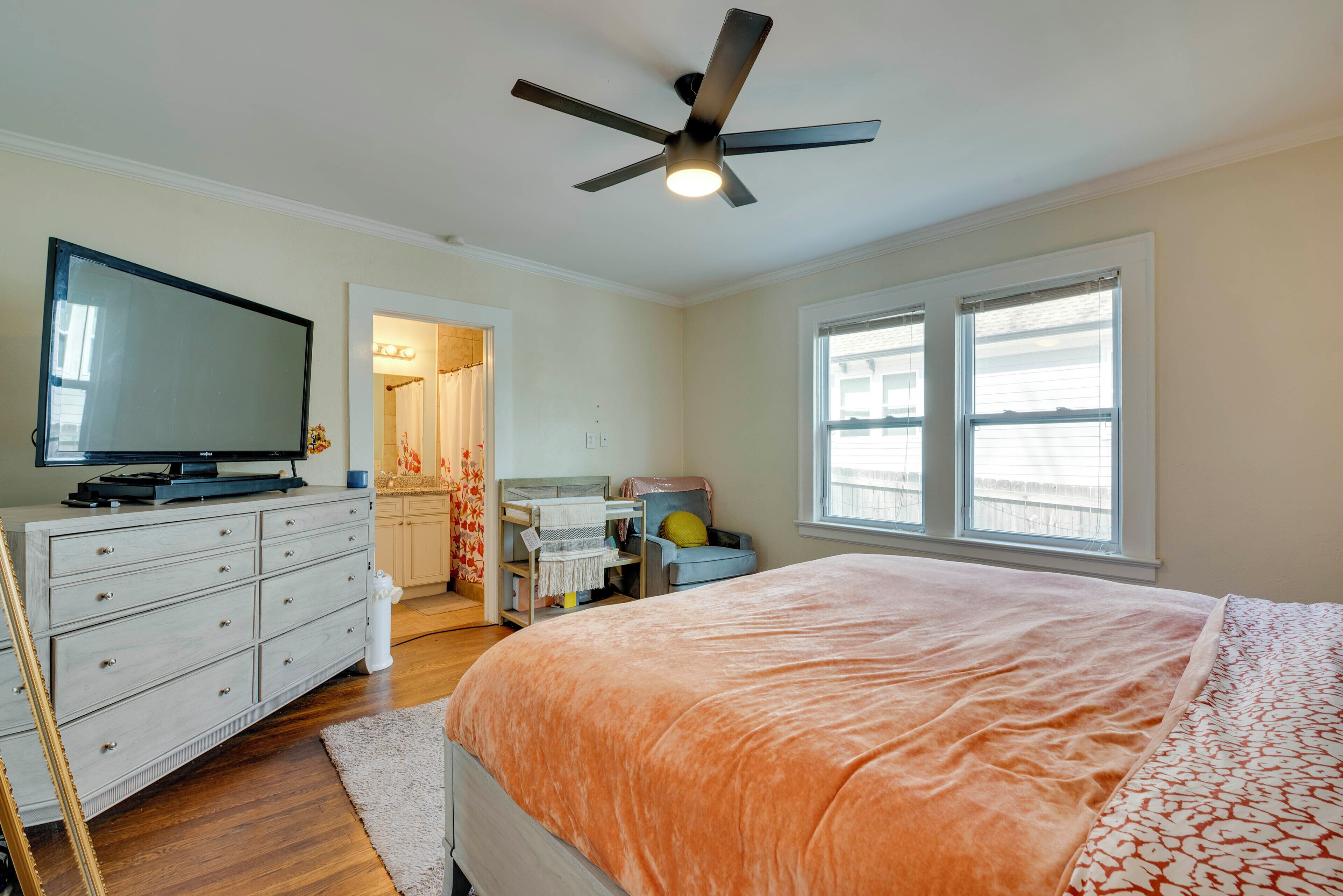 Un dormitorio con cama, cómoda, televisor sobre la c ómoda, ventilador de techo y ventana con persianas.