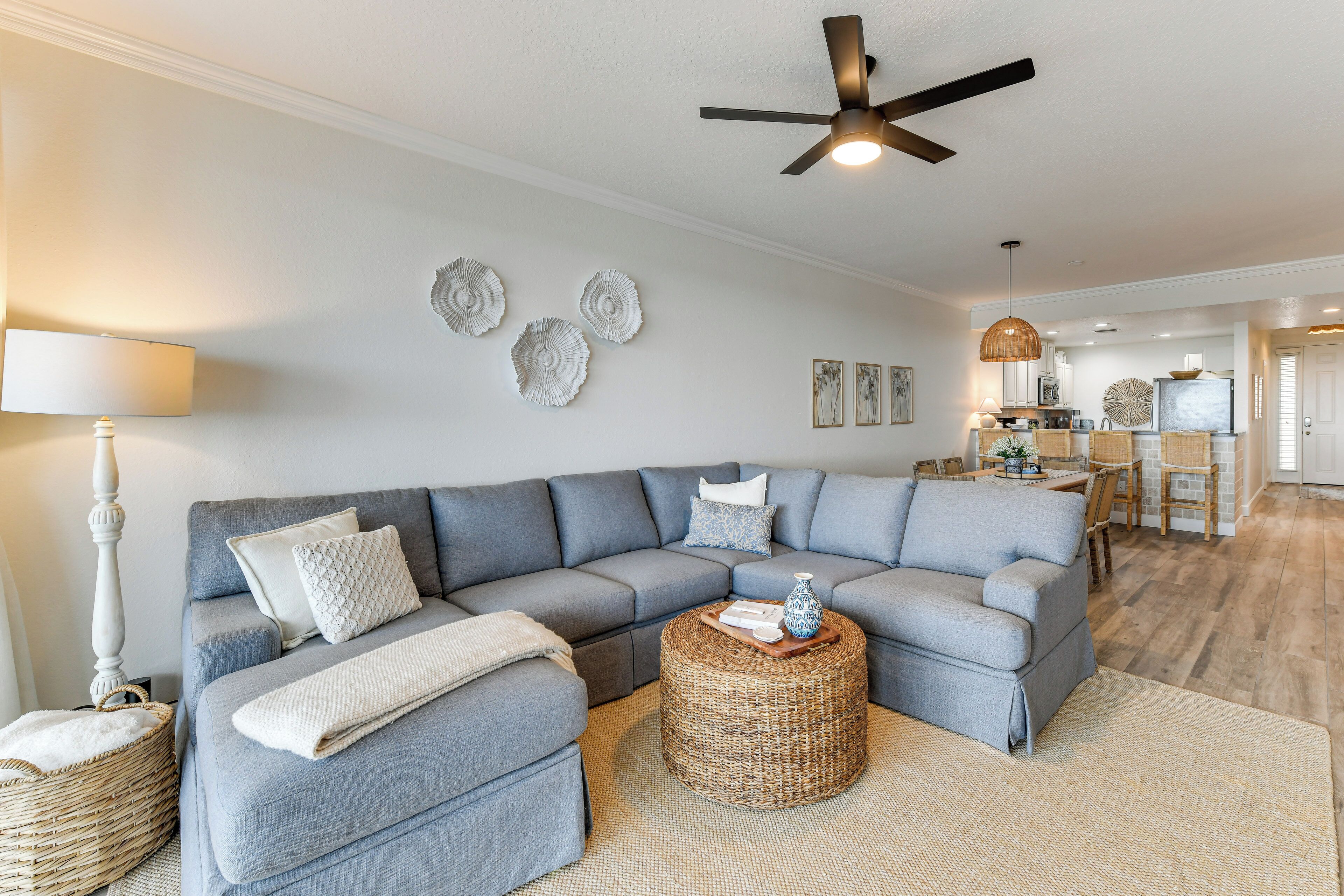 A living room with a grey sectional sofa, a round wicker coffee table, and a ceiling fan.