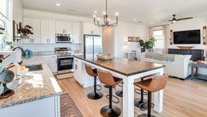 A modern kitchen with white cabinets, a central island with bar stools, stainless steel appliances, and a large TV mounted on the wall. - Oceanfront Retreat in Flagler Beach! Bright Apt (Flagler Beach)