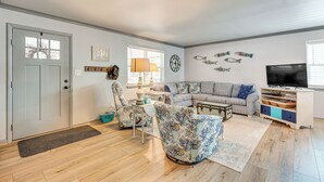 Ein Wohnzimmer mit einer Couch, Sesseln, einem Couchtisch, einer TV-Konsole und Wanddekoration.