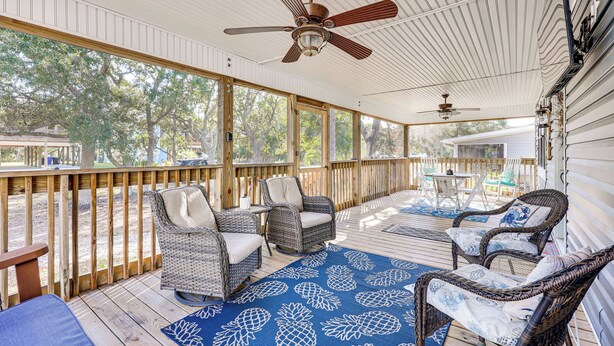 Eine überdachte Veranda mit Korbmöbeln, Deckenventilator und einem blauen Teppich mit Muster.