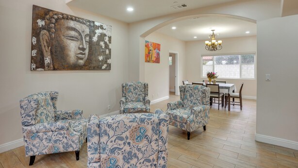 A spacious living room with patterned armchairs, a Buddha painting, and a dining area with a chandelier. - Explore the OC Coast! Midway City Home w/ Yard (Midway City)