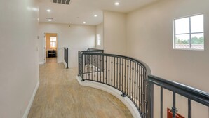 A spacious hallway with a curved staircase, wooden flooring, and a view of a room with a window. - Explore the OC Coast! Midway City Home w/ Yard (Midway City)