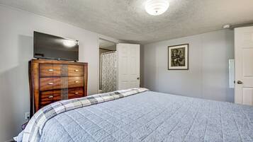 A bedroom with a large bed, a wooden dresser, a flat-screen TV, and a door leading to another room.