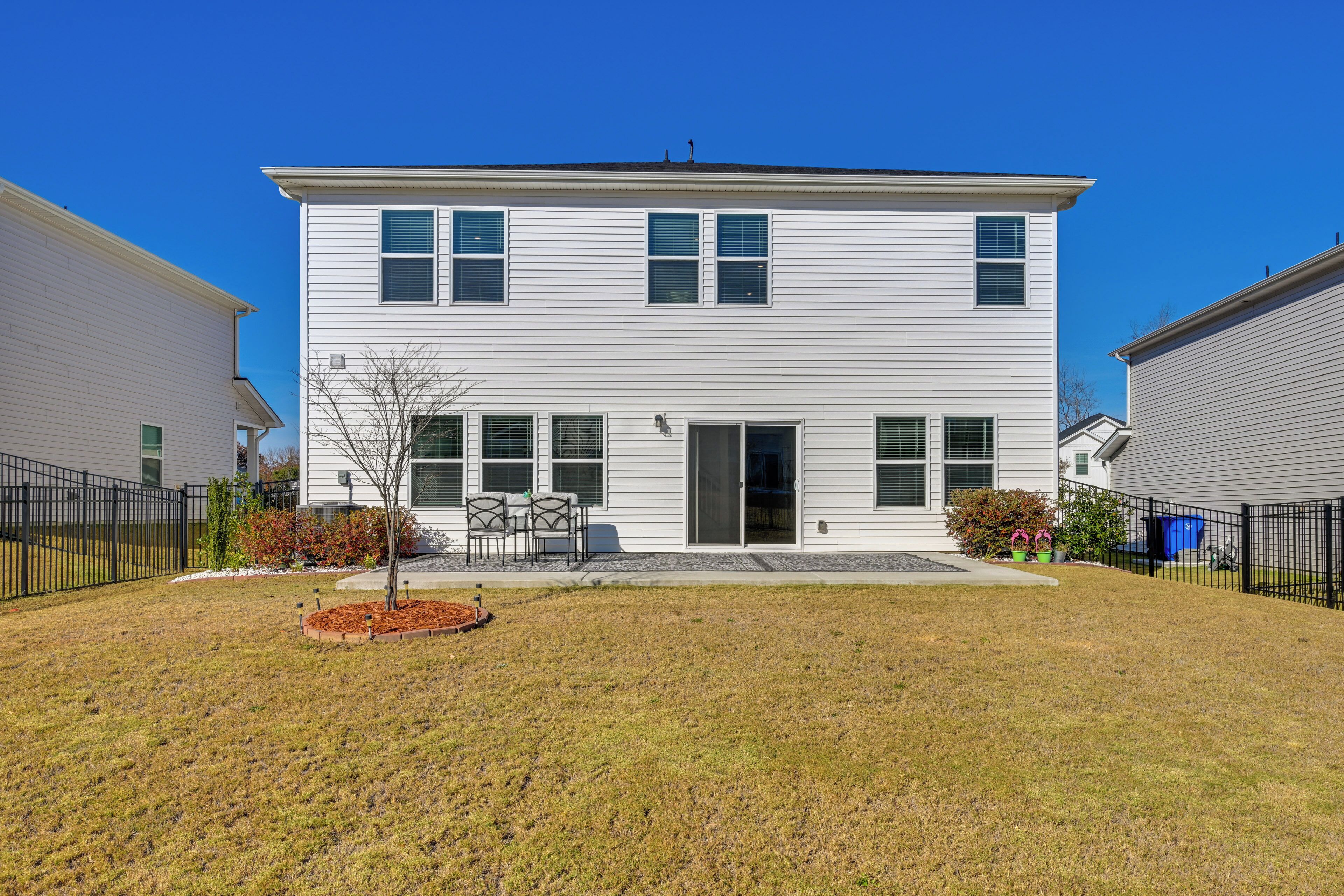 A two-story house with a front door, a small patio with a table and chairs, and a fenced yard.