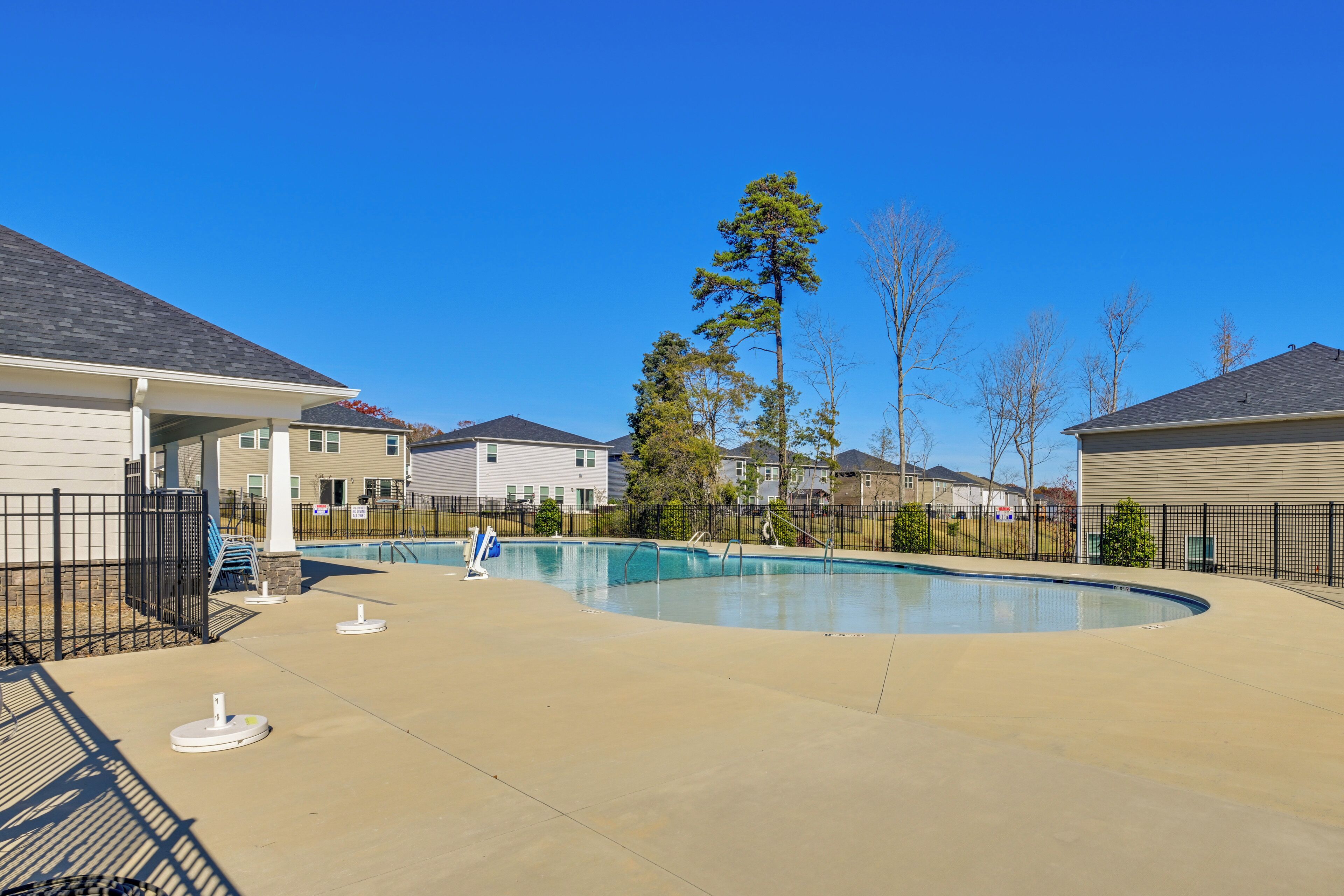 A swimming pool area with a curved pool, a covered seating area, and a fence.