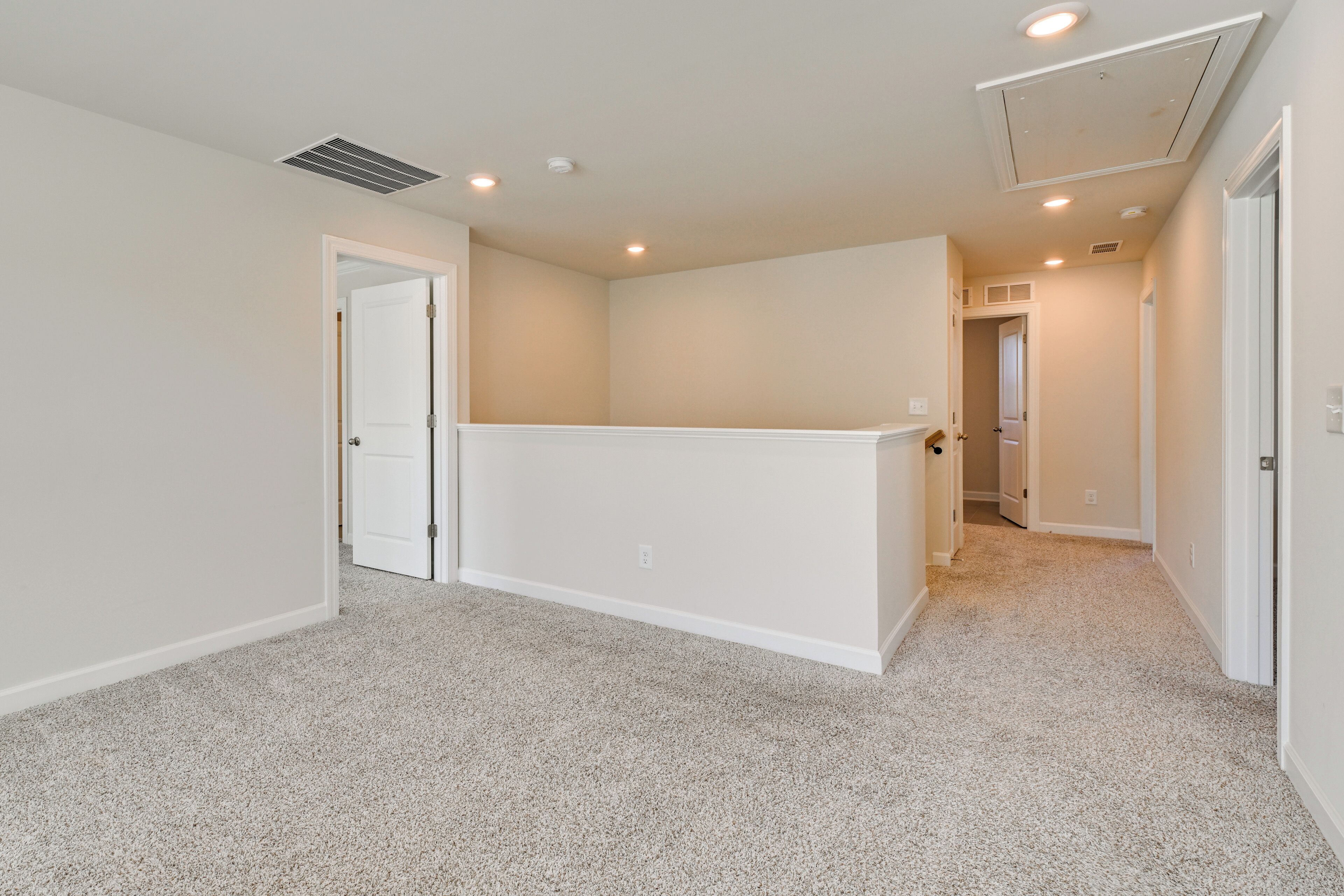 A spacious room with carpeted flooring, white walls, and a ceiling with recessed lighting.