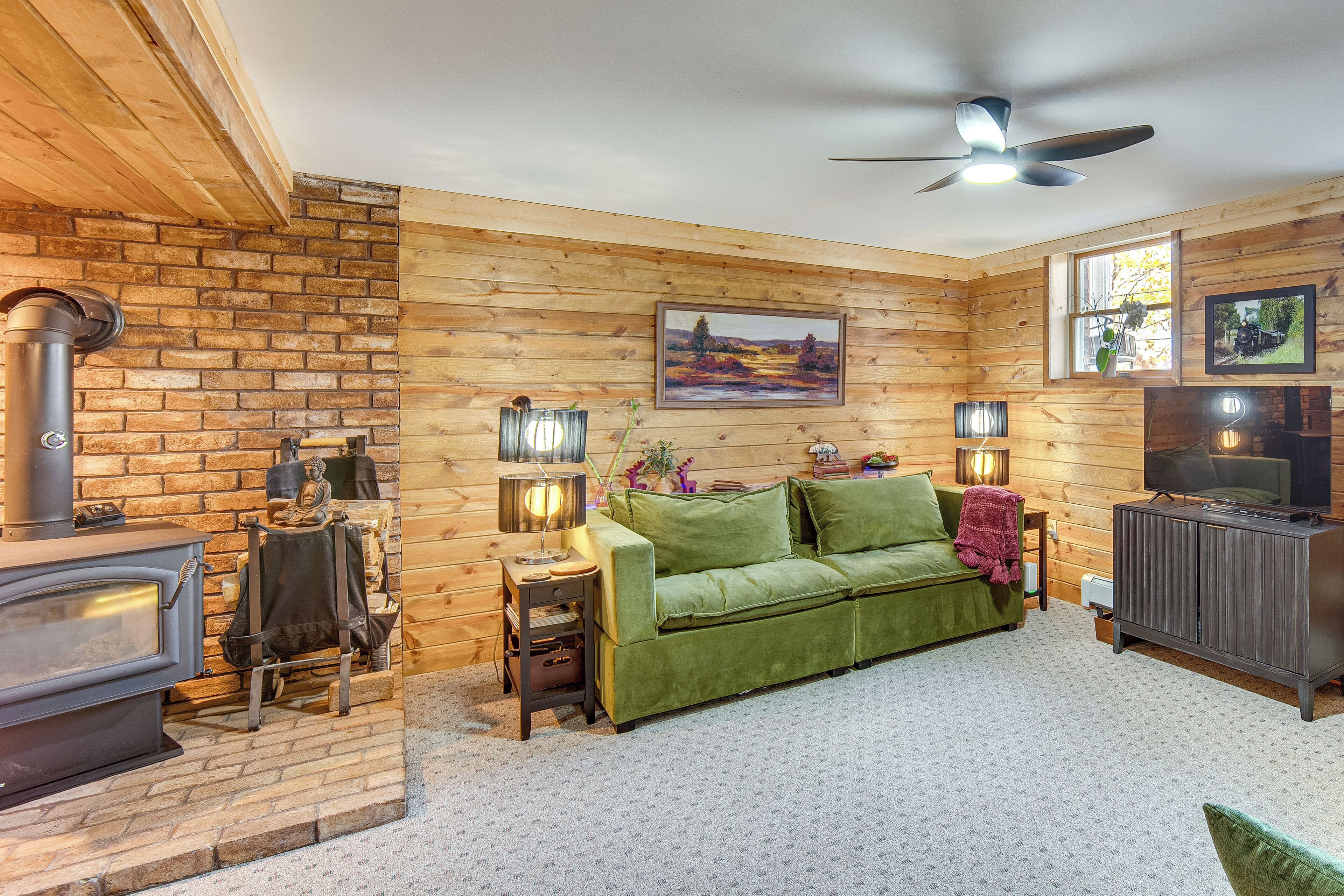 Una sala de estar acogedora con un sofá verde, una chimenea, un televisor y paredes de madera.