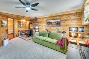 Ein gemütliches Blockhaus-Interieur mit einem grünen Sofa, einem Kamin und einem Deckenventilator.