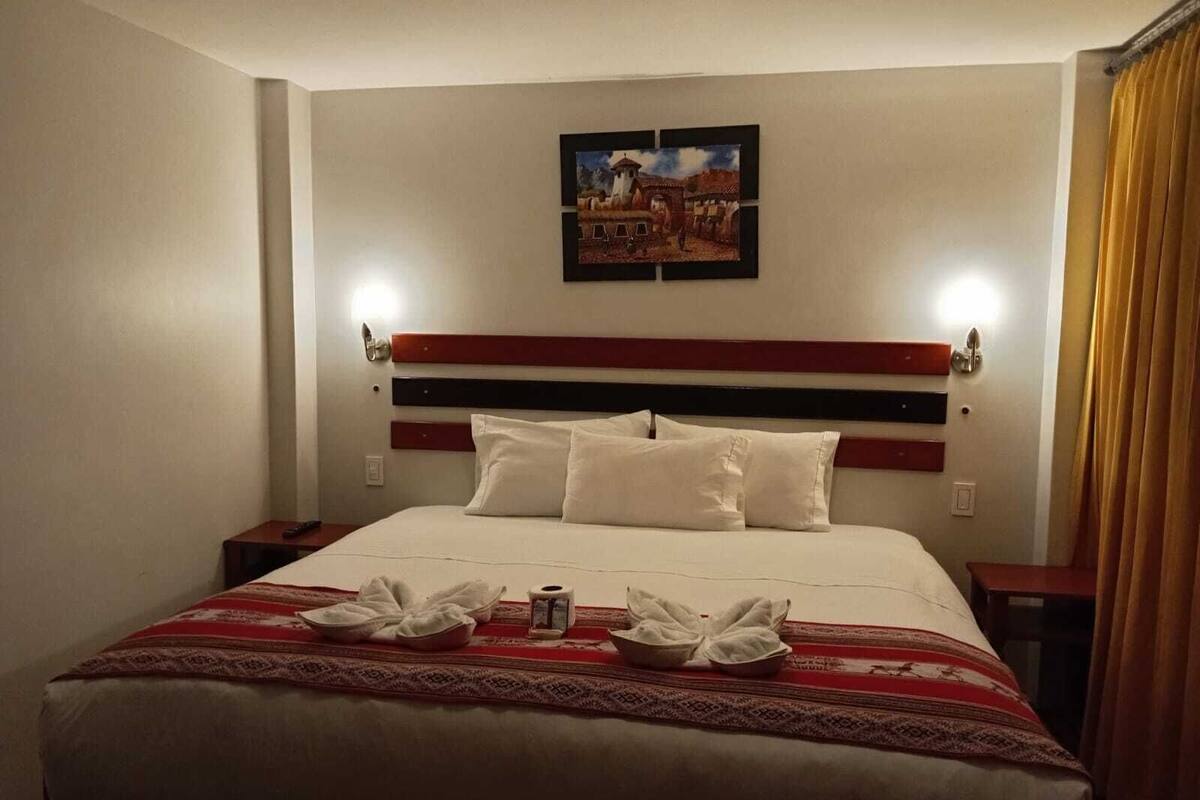 A hotel room with a bed, a painting on the wall, and a window with curtains.