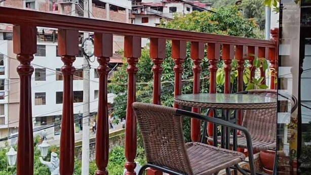 A balcony with a red railing, two wicker chairs, and a small round table. - Raymi MachuPicchu (Aguas Calientes)