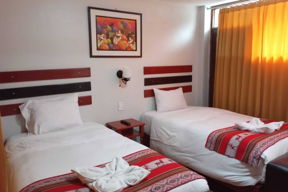 A hotel room with two beds, a painting on the wall, and a window with curtains.