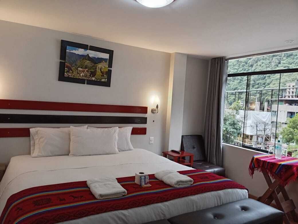Ein Hotelzimmer mit einem großen Bett, einem Kopfteil, einem Nachttisch, einem Sessel, einem Fenster mit Blick auf Grünflächen und einem Tisch mit Tischdecke.