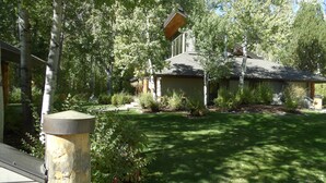 Una casa con techo inclinado, rodeada de un jardín cuidado y árboles altos.