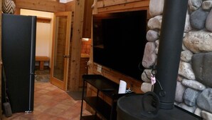 Una habitación acogedora con pared de piedra, estufa de leña negra, televisión y refrigerador.
