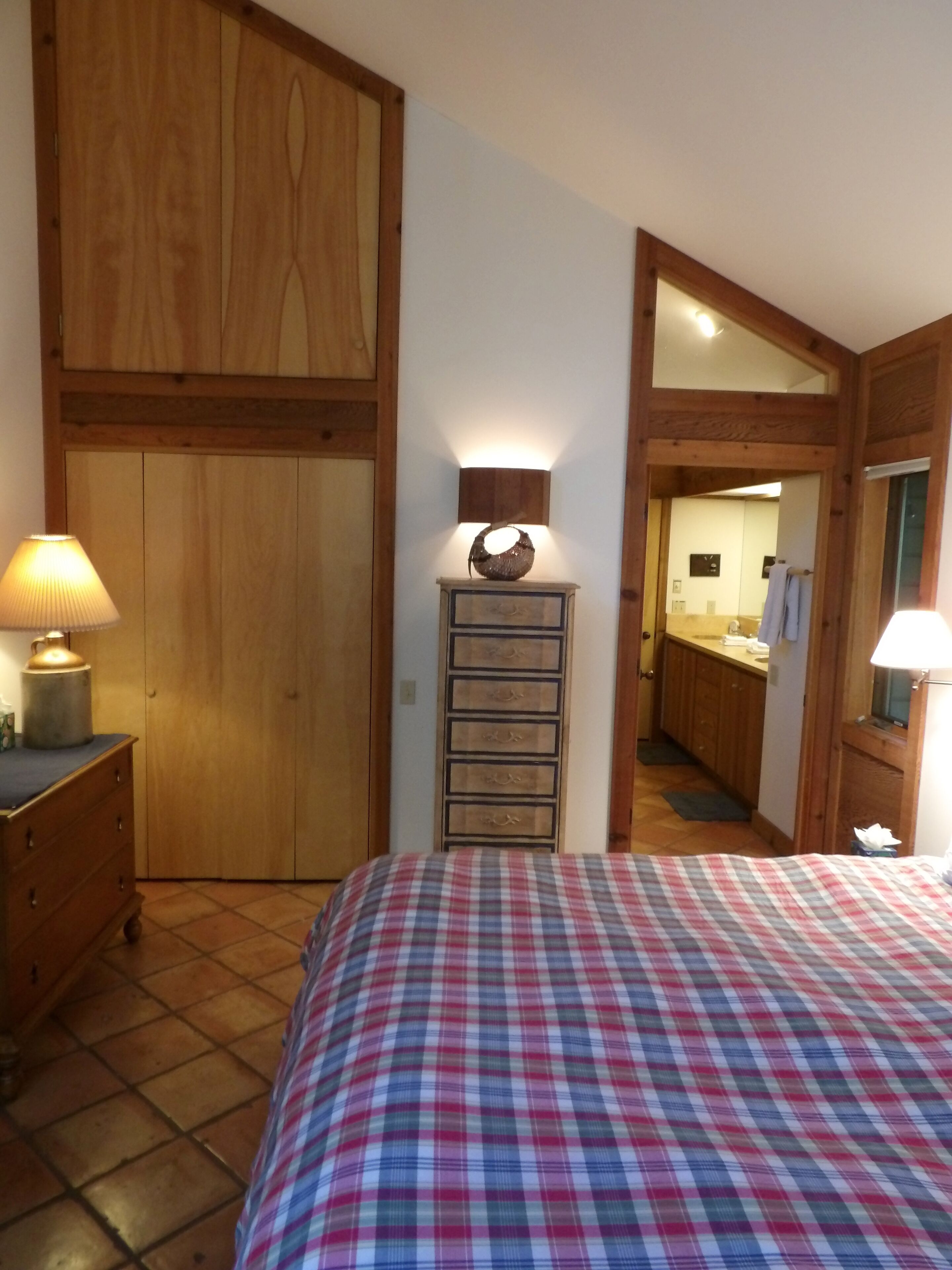 Une chambre à coucher avec une couvre-lit à carreaux, une armoire en bois et une lampe de chevet.