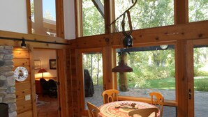 Interior acogedor de una cabaña de madera con una mesa redonda, sillas, un reloj y una pared de piedra.