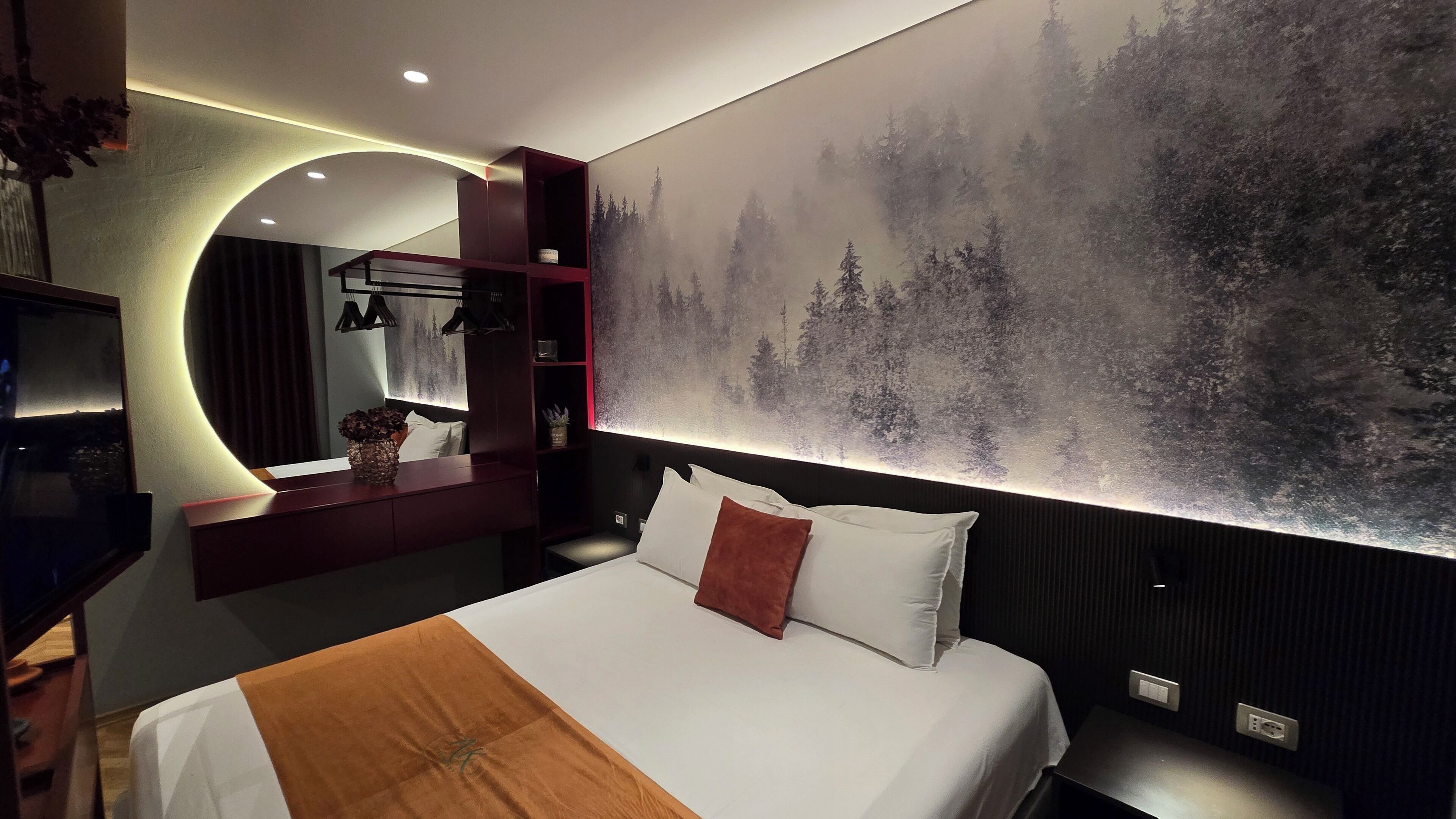 Ein modernes Hotelzimmer mit einem großen Bett, einem an der Wand montierten Fernseher und einem großen Waldgemälde.