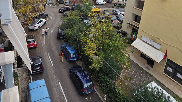 Une rue résidentielle bordée de voitures garées et d’immeubles.