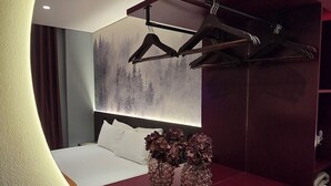 Een moderne slaapkamer met een gebogen plafond, een bed met witte lakens, een rode console tafel en een wandplank met kleding.