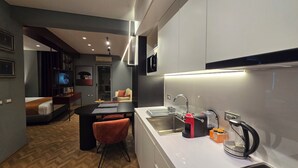 Een moderne keuken met een inbouwoven, een koffieapparaat en een spoelbak. Er is een eethoek met een tafel en stoelen, en een woonkamer met een bank en een televisie.