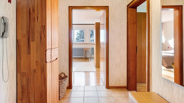 A hallway with wooden doors, a tiled floor, a wicker basket, and a view into a room with a bed and window. - Apartment 3 with Shared Garden and Wi-Fi (Lenzkirch)