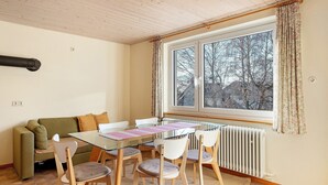 A room with a glass table, white chairs, a green sofa, and a window with curtains. - Apartment 3 with Shared Garden and Wi-Fi (Lenzkirch)