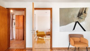 A room with a wooden floor, a bed with a yellow headboard, a wooden wardrobe, a small bedside table, and a wall-mounted abstract painting. - Apartment 3 with Shared Garden and Wi-Fi (Lenzkirch)