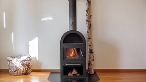 A wood-burning stove with a fire, a basket of firewood, and a birch log against a wall. - Apartment 3 with Shared Garden and Wi-Fi (Lenzkirch)