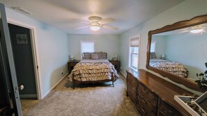 A bedroom with a bed, dresser, mirror, ceiling fan, and a window.